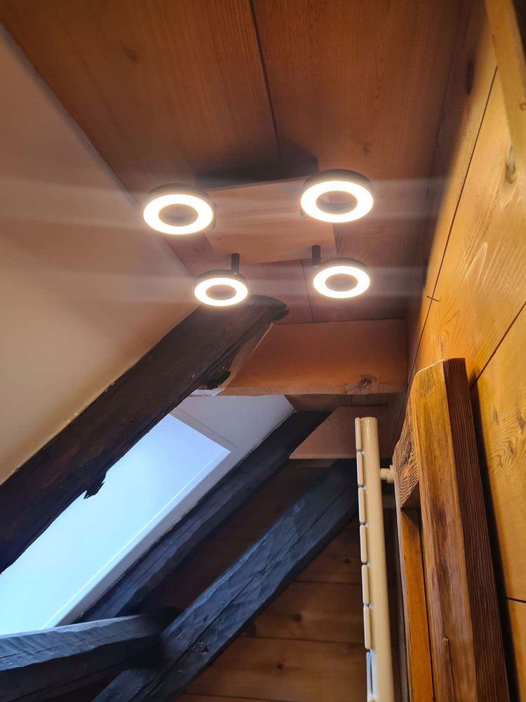 Plafonnier design à anneaux LED installé sous une charpente en bois ancien
