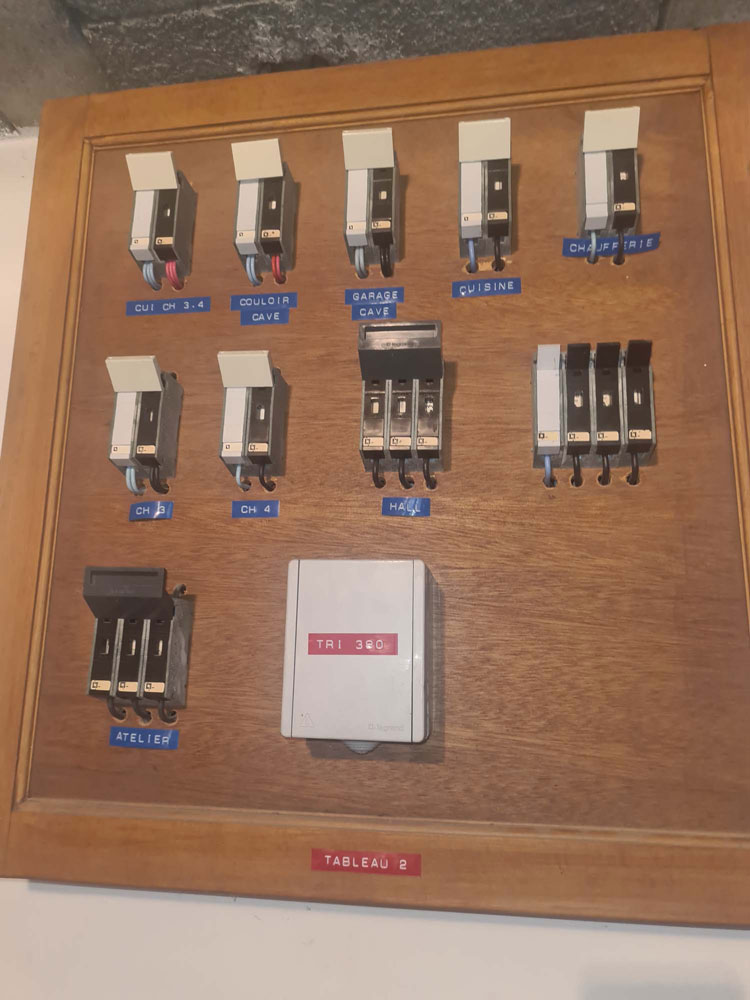 Ancien tableau électrique sur support bois avec étiquettes manuscrites par pièce