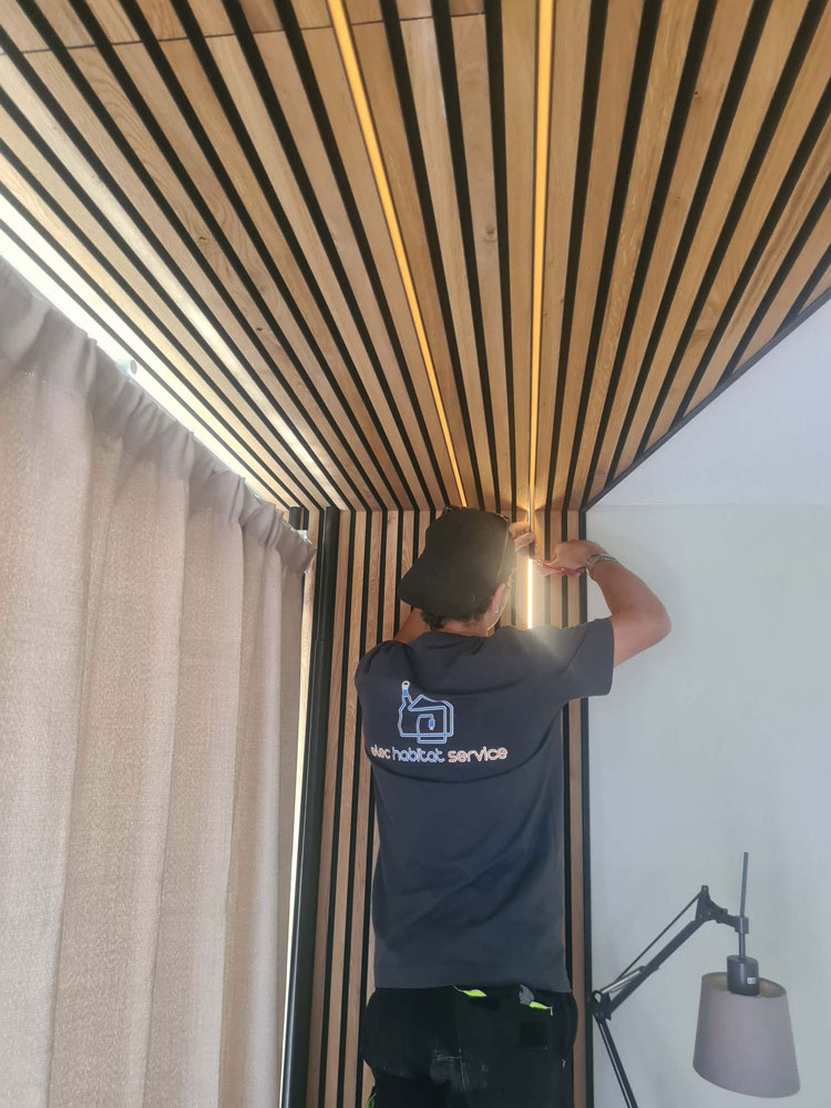 Technicien Elec Habitat Service installant un ruban lumineux LED dans un plafond à claustra bois