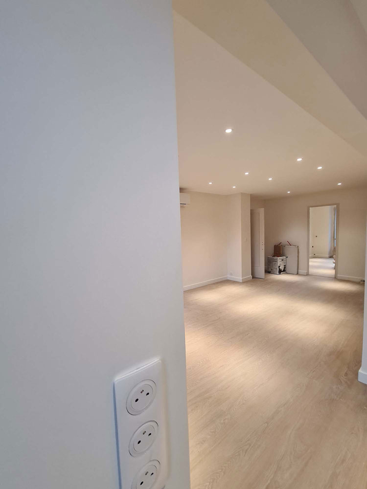 Grand salon rénové avec éclairage encastré, climatisation et baie vitrée donnant sur un balcon
