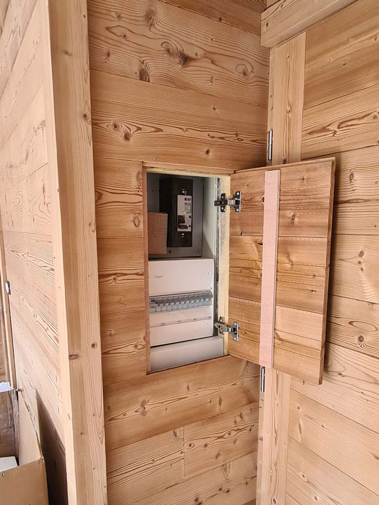 Coffret électrique extérieur étanche installé sur un mur en béton, près d'un chalet